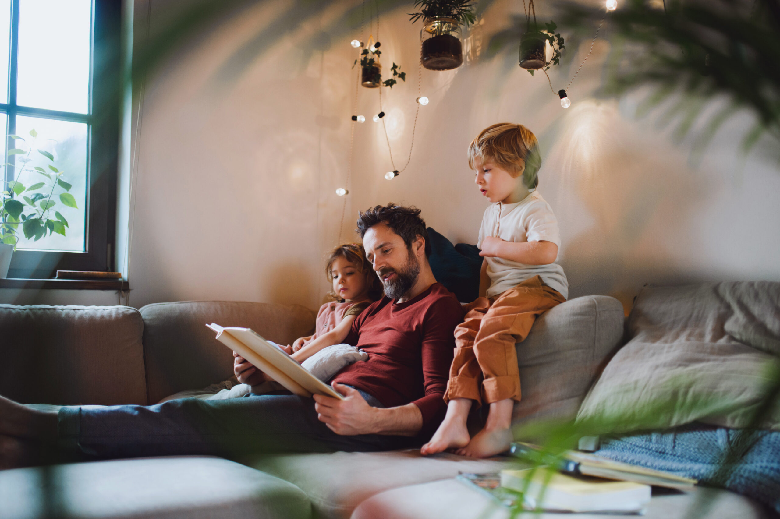 Mature father with two small children resting indoors at home, looking at photo album.
