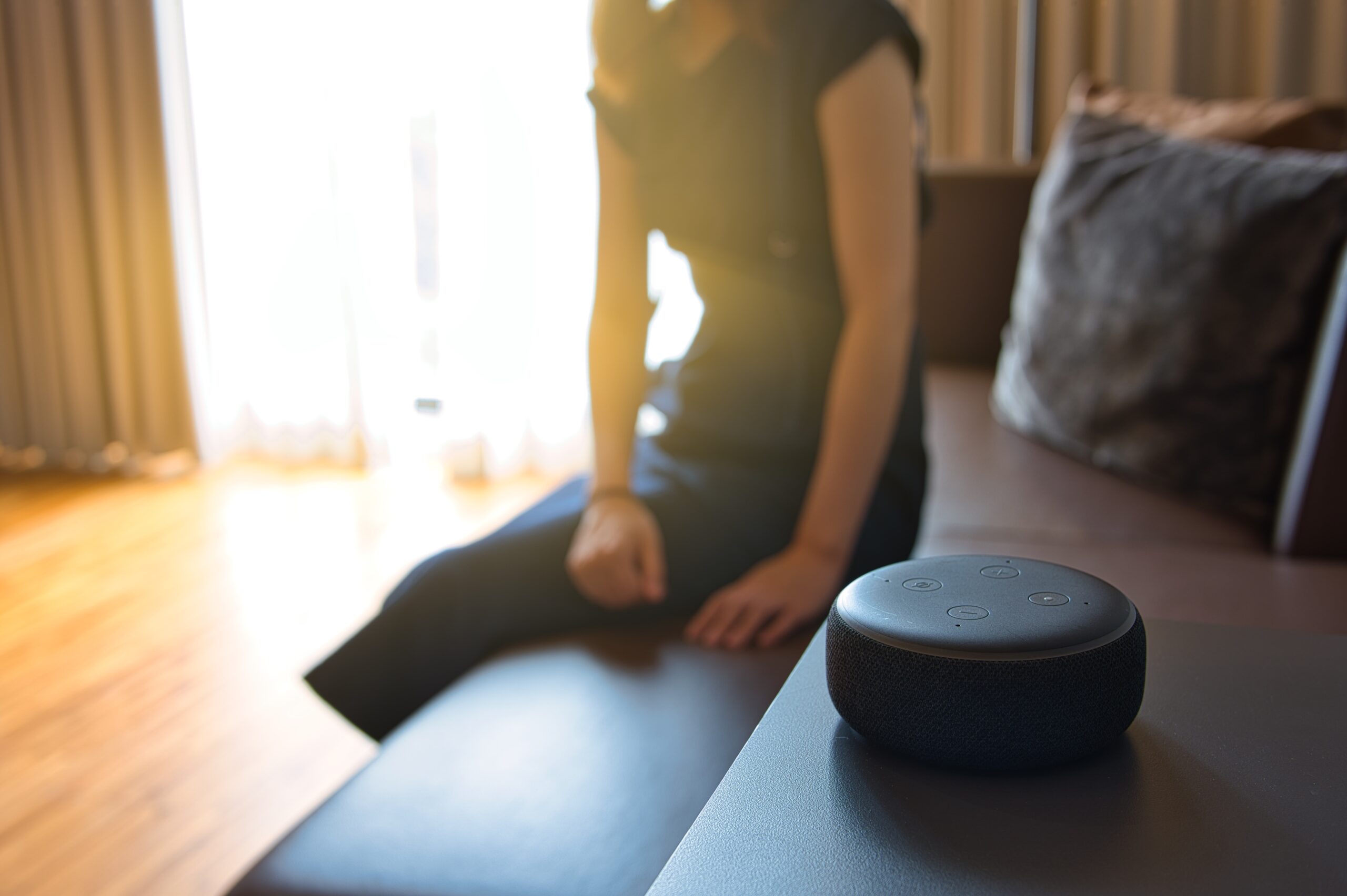 Woman sitting on a chair and talking to a speech recognition device, Amazon Alexa with sunlight background